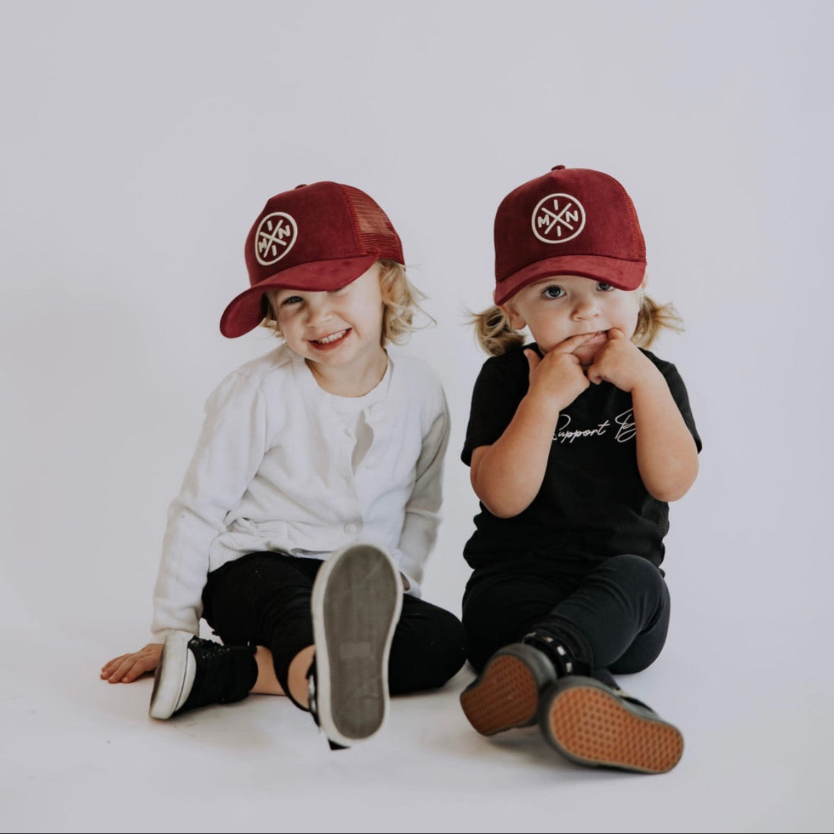 Two children wearing red caps with a logo on a white background
