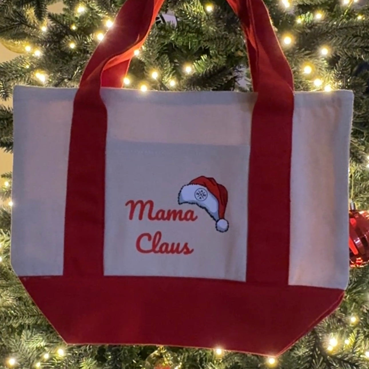 The Mama Claus Tote Bag by Mama X™ Brand is a festive cotton canvas bag with red handles and “Mama Claus” lettering plus a Santa hat—perfect as a holiday errand bag.