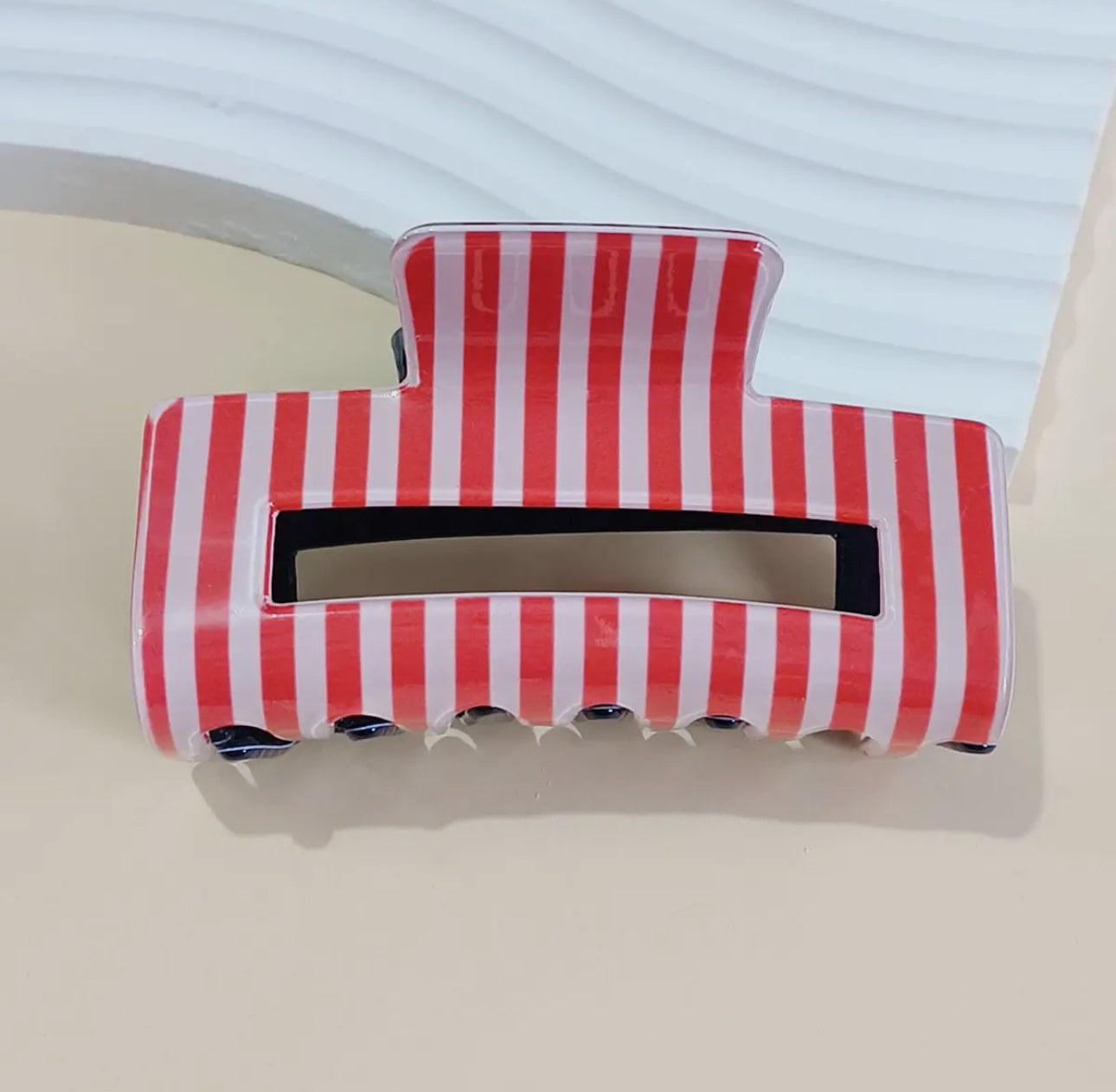 The Mama X™ Brand Red white and blue/Stripe Claw Clip—a large patriotic hair accessory with vertical red and white stripes—rests on a beige surface beside a textured white object.