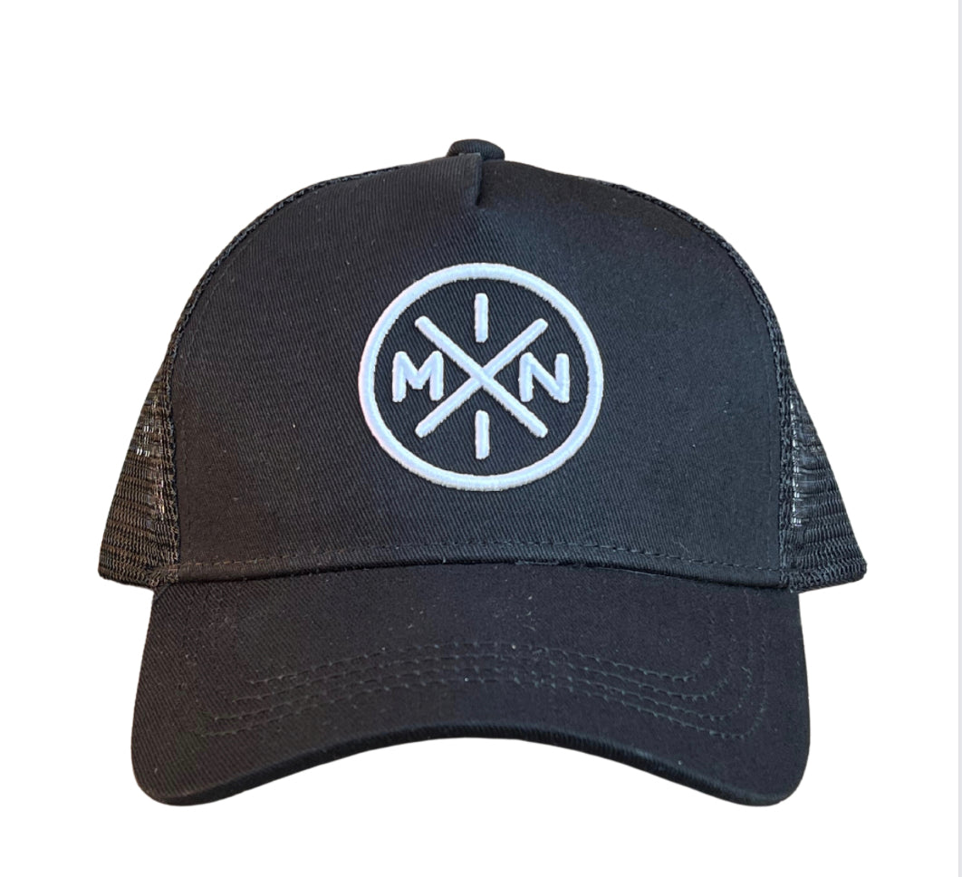 The Mini X Premium Trucker Hat from Mama X™ Brand is a black trucker cap with a mesh back, featuring an embroidered white circular emblem on the front. The emblem contains the letters "M" and "N" separated by intersecting lines that form an "X".
