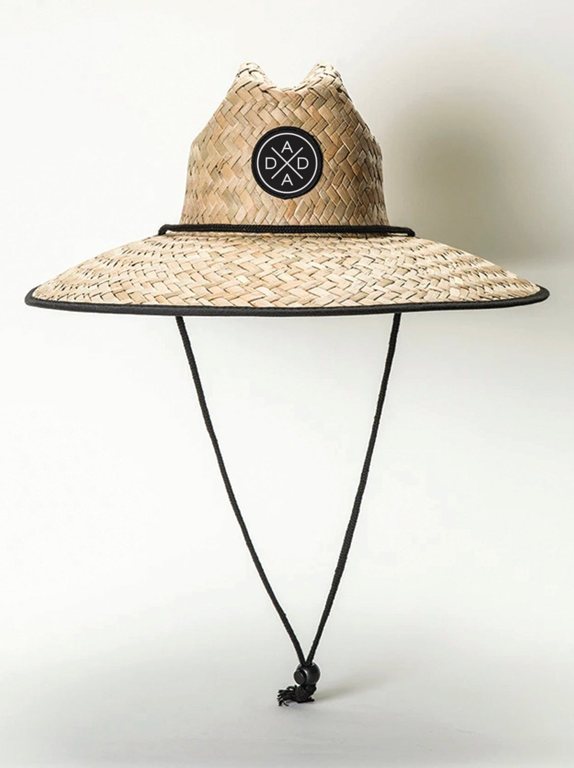 Introducing the Dada X™ Lifeguard Hat by Mama X™ Brand—a stylish, wide-brimmed straw hat featuring an intricate woven design and a black chin strap. The crown is embellished with a black circular patch showcasing a white geometric design at its center. The brim is elegantly edged with black trim, providing both sophistication and sun protection. Set against a plain, light-colored background, this hat makes a chic and functional accessory.