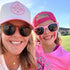 A woman and a young girl in sunglasses smile outdoors on a sunny day. The girl wears a Temecula Softball shirt and the Pink Mama X™ Baseball Cap by Mama X™ Brand, with a grassy field and blue sky making for a cheerful scene.