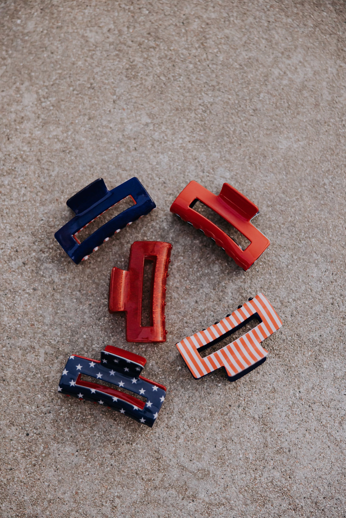 Five Mama X™ Brand hair clips are arranged on a textured surface, featuring the Red White and Blue/Star Claw Clip—perfect for strong hold and festive, patriotic hairstyles.