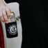 A hand is holding a canned drink wrapped in a black koozie. The koozie, perfect as a gift for Dad, has a white circular logo with the text "Dad Mafia" and "LDC Local Dads Club" on it. This stylish accessory is from the Mama X™ Brand and is named the Dad Mafia Koozie. The background is indistinct.