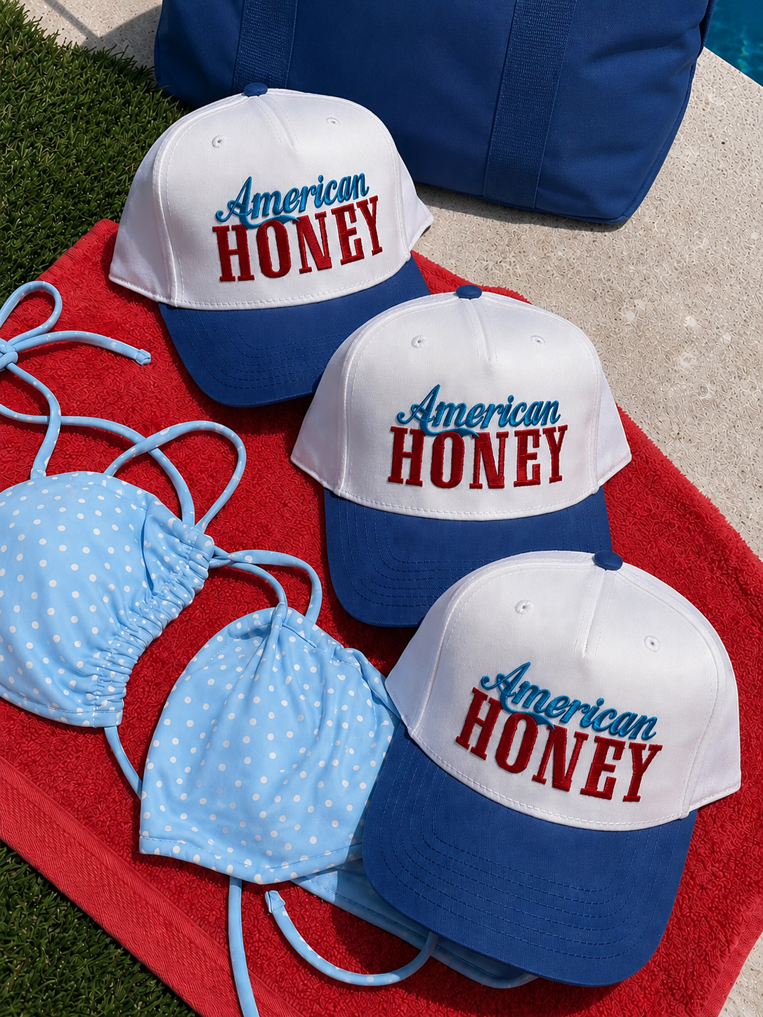 Three Mama X™ Brand "American Honey" white and blue baseball caps with red and blue text are on a red towel by the pool, next to a blue polka-dot bikini and a blue bag.