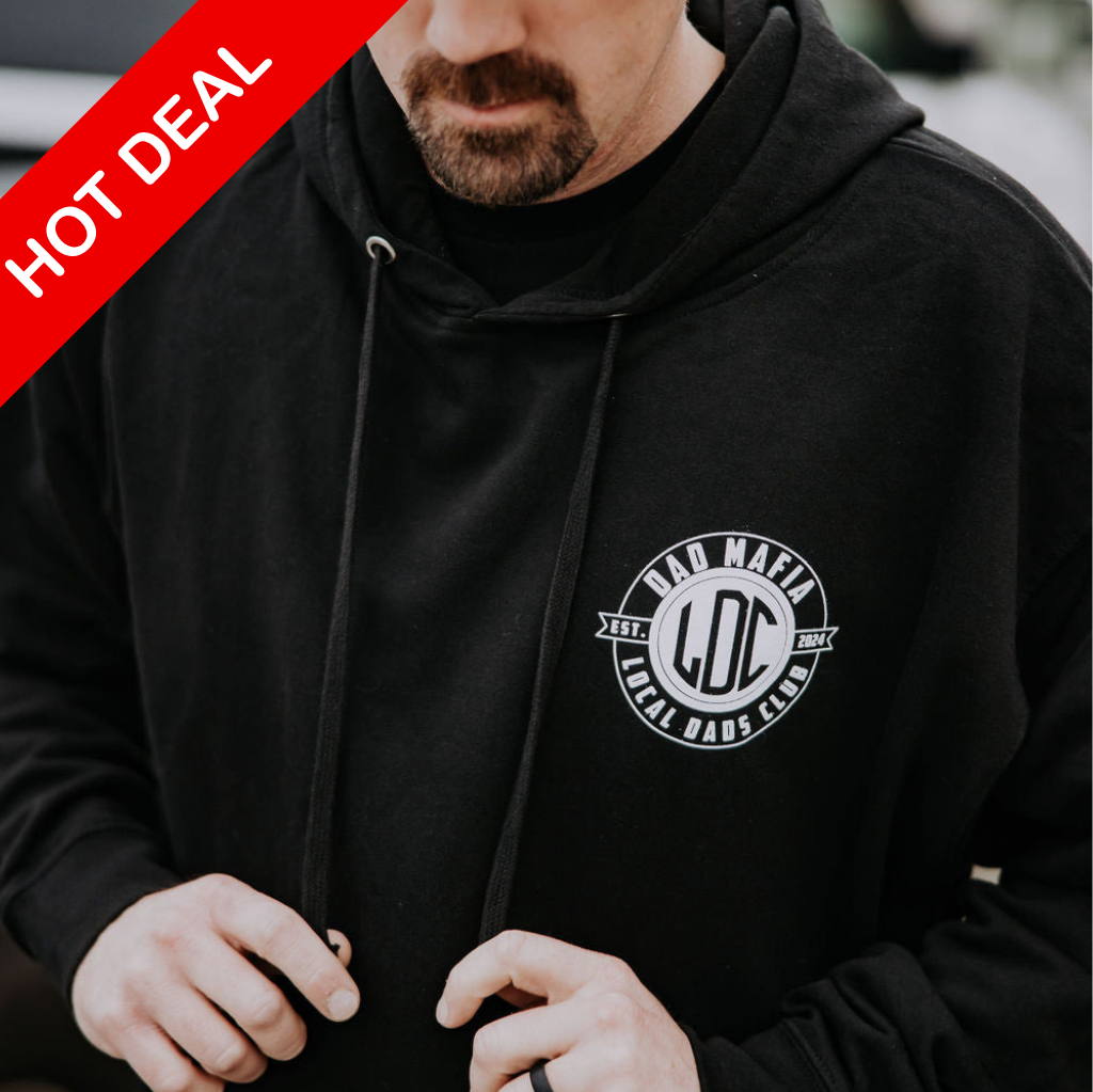 A person wearing a black, heavy-weight Dad Mafia Hoodie by Mama X™ Brand is adjusting the drawstring. The fleece-lined hood provides added comfort and warmth. A red banner with the text 