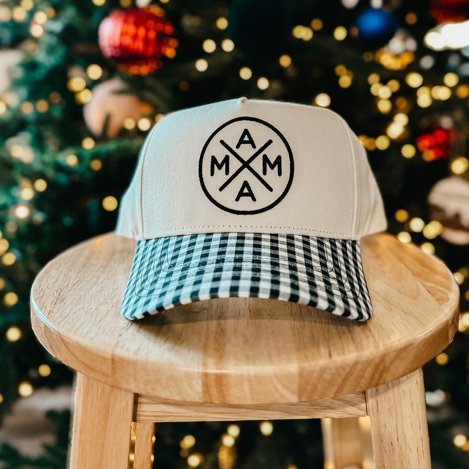 Trucker hat with checkered front panel on a wooden stool in front of a decorated Christmas tree.