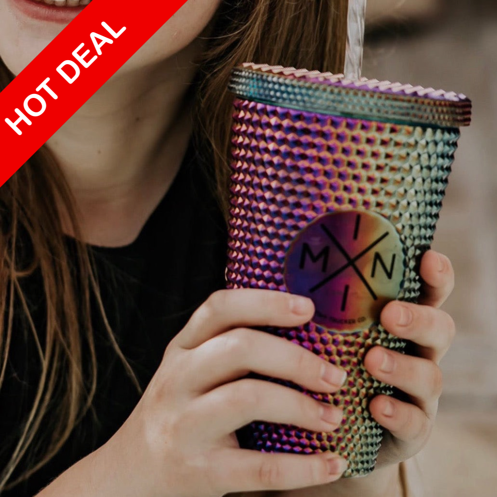 A person holds a vibrant Mini X Studded Plastic Tumbler 16oz from Mama X™ Brand, filled with a refreshing drink. The tumbler features a circular logo and includes a BPA-free, reusable metal straw. A red banner in the top left corner announces, 