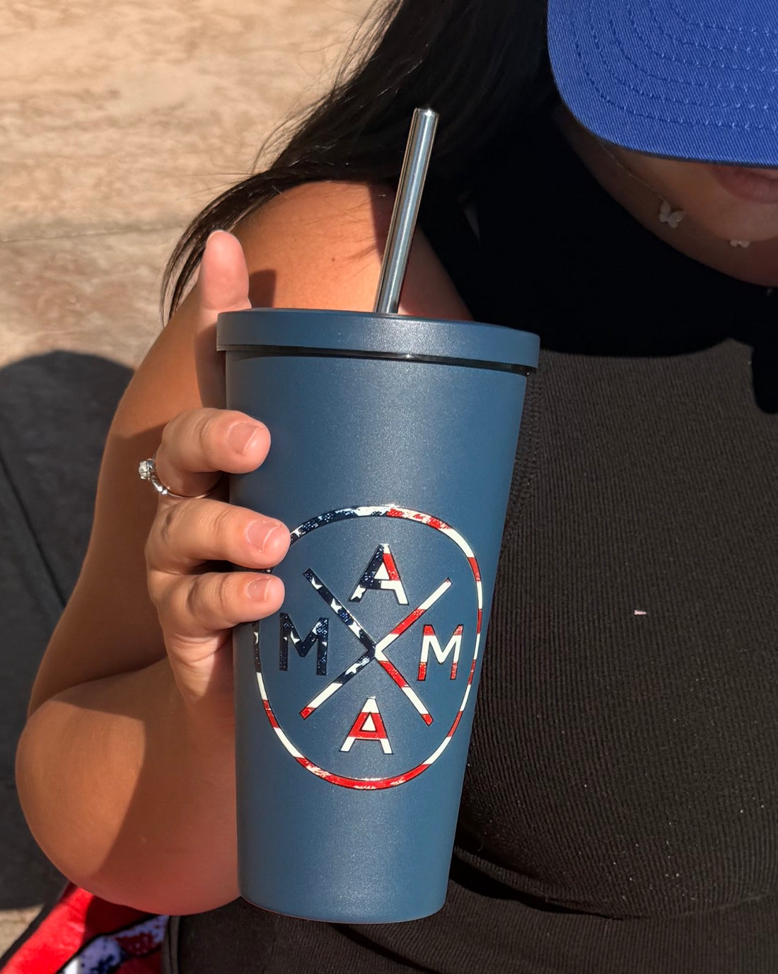 A woman in a black sleeveless top and blue cap holds the Mama X™ Brand&