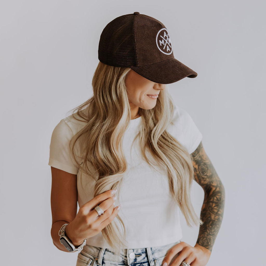 Woman wearing a brown cap with a logo, white t-shirt, and denim shorts on a plain background