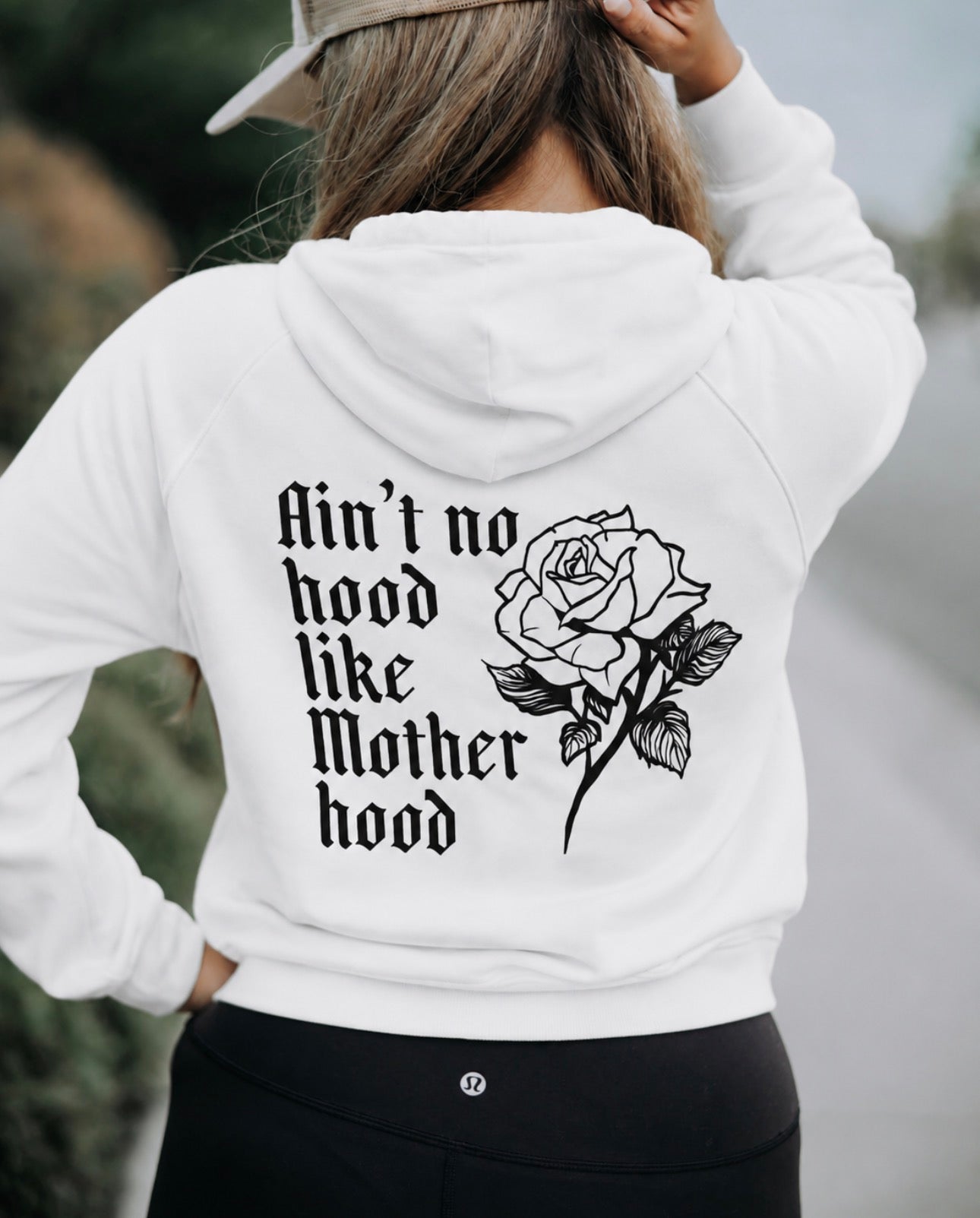 A woman stands outdoors, facing away in a Mama X™ Brand Mother Hoodie—regular fit, white with "Ain&