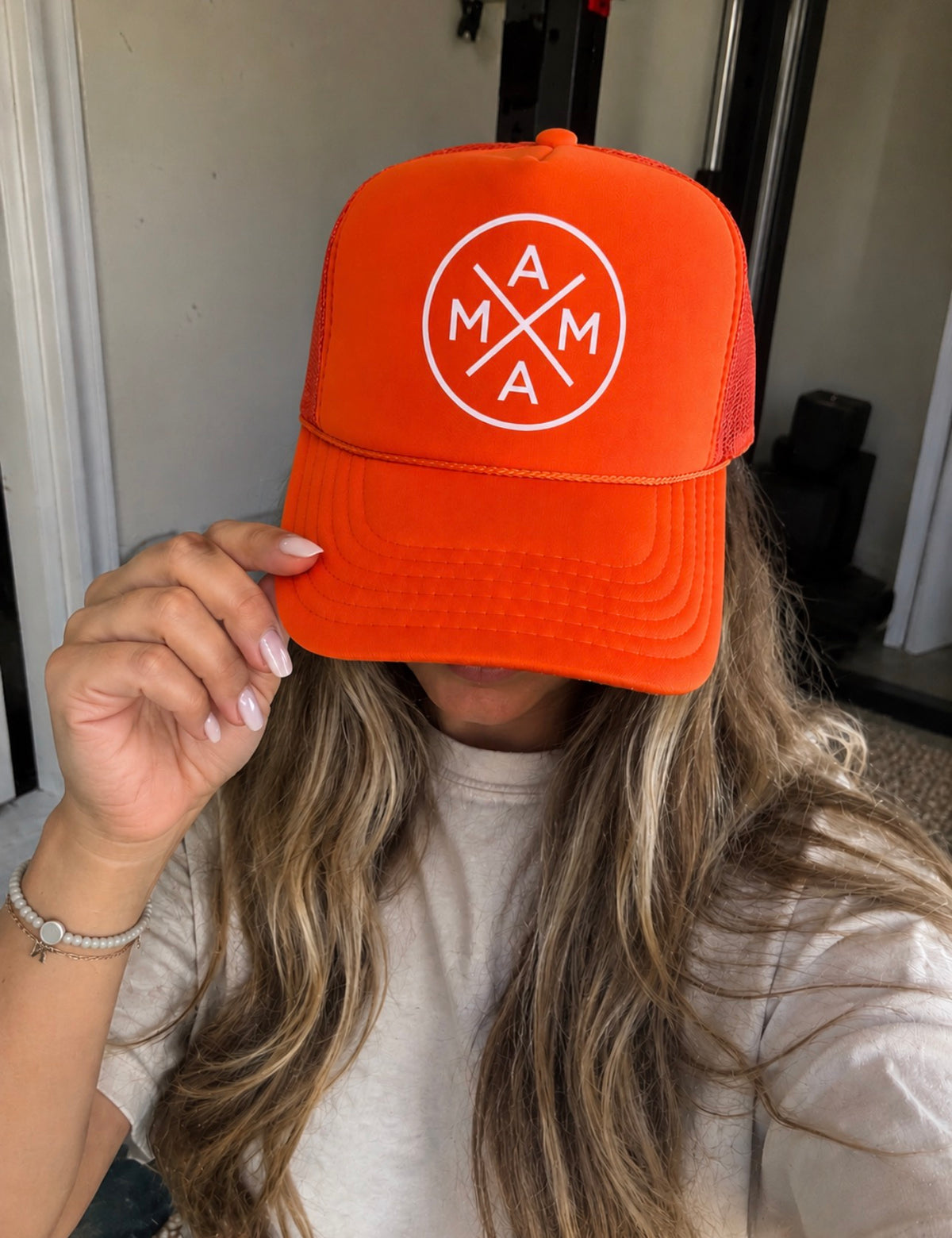 An Orange Mama X foam trucker hat featuring a white circular logo with the word “MAMA” arranged in a cross pattern.