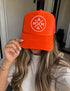 An Orange Mama X foam trucker hat featuring a white circular logo with the word “MAMA” arranged in a cross pattern.