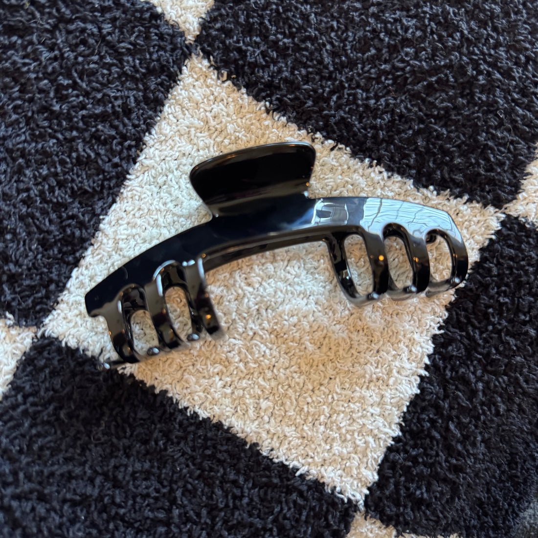 A Black Trucker Claw Clip from Mama X™ Brand rests on a textured, black-and-white checkered surface.