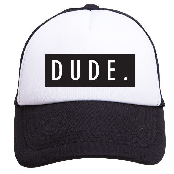 The Dude Trucker Hat, by Mama X™ Brand, is a stylish boy's cap featuring a white and black 5-panel design. It showcases a black rectangular patch with the word "DUDE." in bold white uppercase letters on the front. The hat includes a curved visor and detailed black stitching, adding to its trendy appearance.