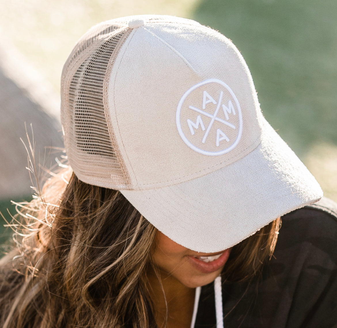 A person wearing a Mama X™ Light Suede Trucker Hat with a beige mesh back and a patch that reads 