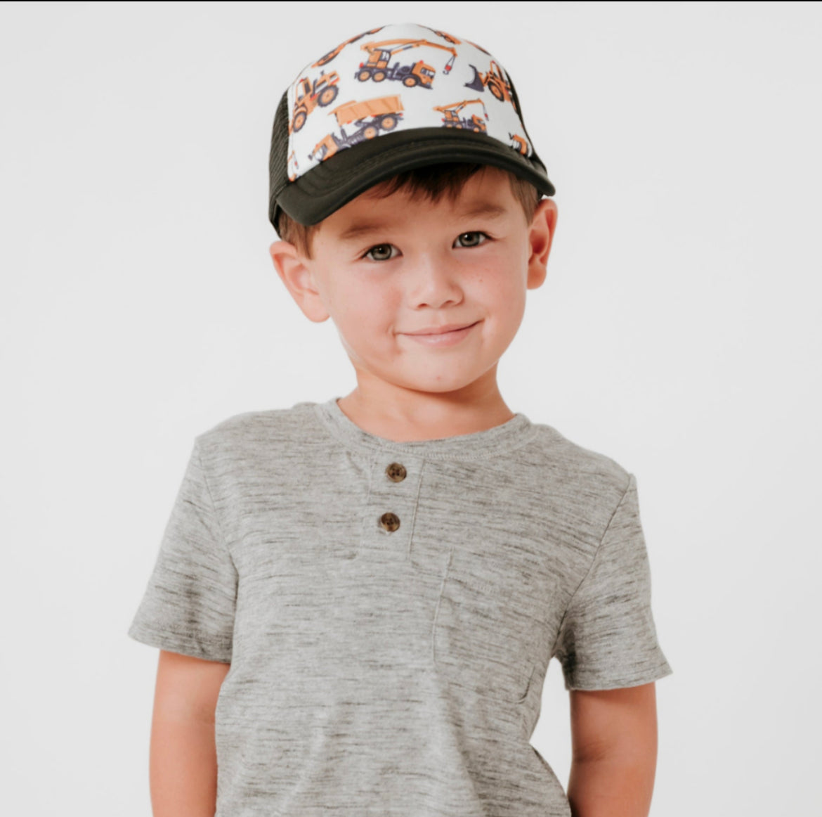 Boy playing wearing a black trucker hat with white canvas and yellow tractors 