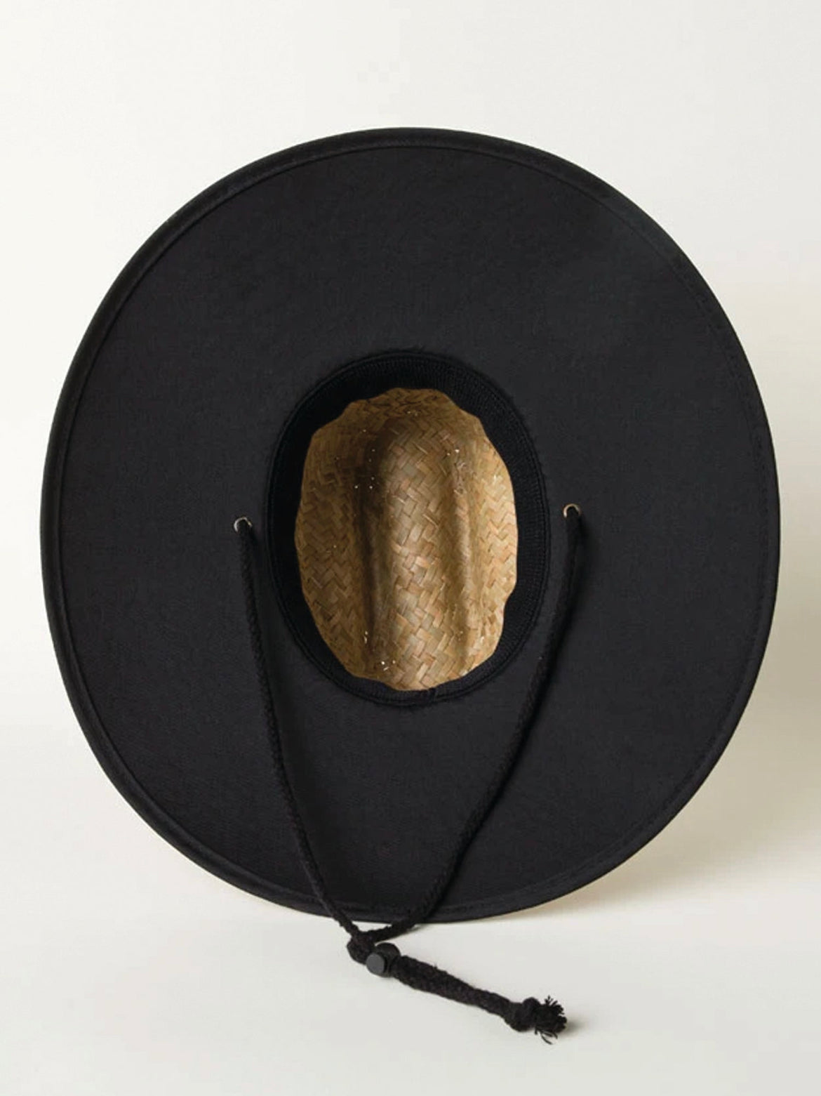 The Dada X™ Lifeguard Hat from Mama X™ Brand, a black, wide-brimmed straw hat with a woven interior and black chin cord, lies against a plain white background. This stylish hat features a round crown opening and two metal eyelets flanking the cord ends, offering both sun protection and timeless elegance.